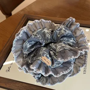 Denim fabric lace scrunchie close-up detail showcasing ruffled edge and cute leather tag design.