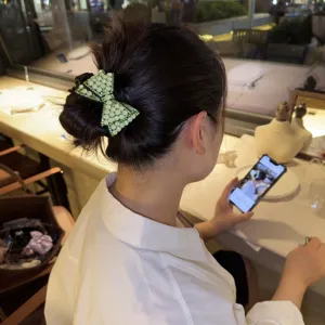 Vista dettagliata dell'accessorio per capelli con fiocco di perle verdi indossato con stile.