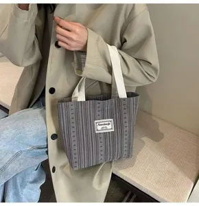 Detail view of a stylish grey striped corduroy tote bag with white handles for daily commute.
