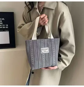 Detailed view of striped canvas tote bag with white handles and brand label in daily use.