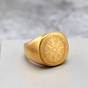 Primer plano de los detalles del anillo de sello de brújula de acero dorado mate grabado.