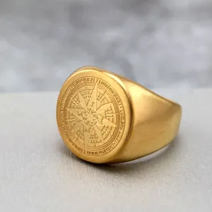 Primer plano detallado de un anillo de sello vintage de acero dorado con diseño de brújula.