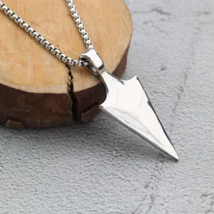 Détail en gros plan d'un pendentif flèche en acier inoxydable rétro sur support bois.