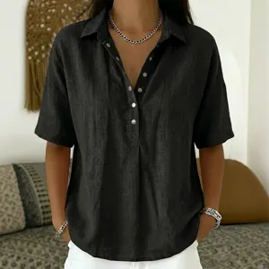 Close-up detail of black short-sleeve lapel button-down blouse worn by model in room setting.