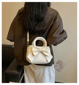 Detail shot of a chic white leather handbag featuring a large bow and top handle for women.