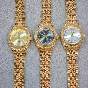 Gold tone women quartz watch detail, shiny metal link bracelet, sparkling rhinestone dial markers.