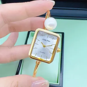 Detailansicht der goldenen Armbanduhr mit Perle und schickem quadratischen Zifferblatt.