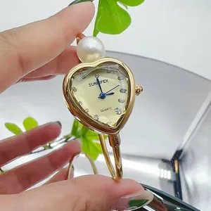 Detailansicht der herzförmigen Quarzuhr mit Perle und elegantem goldenen Armreifarmband.
