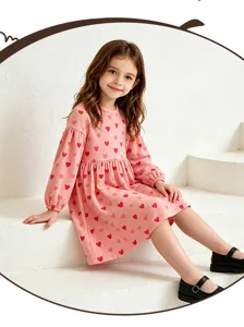 Charming girl long sleeve pink dress with cute red heart prints, posed on white steps detail.