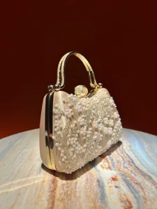 Detailed view of exquisite champagne evening clutch with pearls, beads and gold handle.