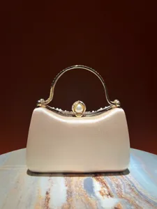 Detailed view of elegant champagne satin evening clutch bag with pearl rhinestone clasp and gold handle.
