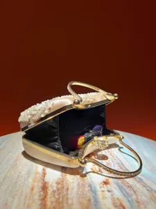 Detailed view of the satin evening clutch bag with pearl embroidery and gold rhinestone handle.