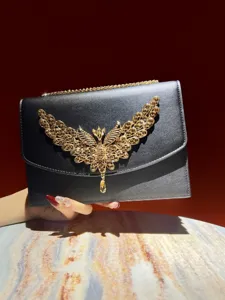 Nahaufnahme der luxuriösen Abendtasche mit goldenen Strass-Flügeln und Metallkette.