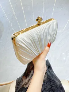 Detailed view of white pleated satin clutch bag with gold metal frame and knot lock clasp.