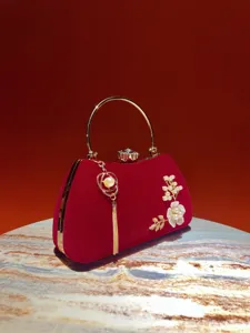 Dettaglio pochette in velluto rosso con manico dorato, nappa di perle e chiusura per banchetto.