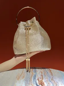 Stunning gold glitter bucket bag with metal top handle and chic chain tassels for evening parties.