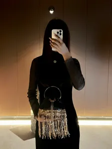 Close-up of luxury black evening bag with metal ring handle and sparkling gold fringe details.