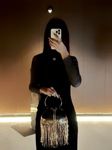 Detailed shot of a stylish black evening bucket bag with luxurious gold fringe and metal handle.