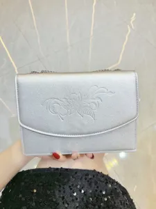 Dettaglio borsa a catena metallica argentata, elegante pochette da donna con motivo floreale impresso.