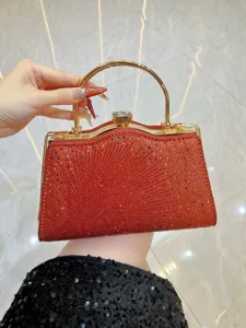 Glitterende rode avondtas detail met gouden metalen handvat en kristallen sluiting.