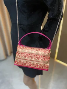 Detailansicht der eleganten roten Abendtasche mit goldener Stickerei und pinkem Griff.