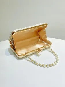 Detailed view of white pleated satin evening clutch bag with pearl handle and gold metal frame.