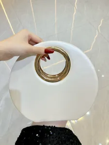 Vue de détail de sac de soirée rond, cuir blanc minimaliste avec poignée anneau doré.