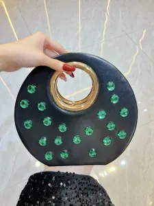 Gros plan détail du sac de soirée rond noir avec poignée anneau doré et cristaux verts.
