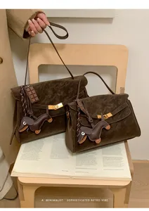 Detailgezicht van retro bruine suède handtas met schattige hangers op een boek.