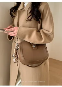 Brown leather saddle shoulder bag detail, stylish crossbody bag with metal clasp and charms.