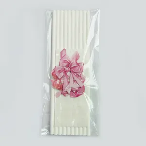 White paper straws with pink bow and cherry decoration, disposable eco-friendly party drinkware.