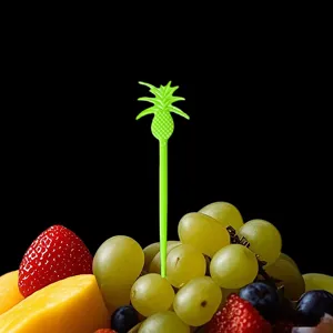 Detailed closeup of a vibrant green plastic pineapple fruit fork inserted in fresh fruit plate.