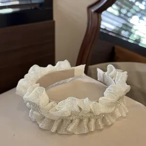 Detailed view of white pleated headband with delicate crystals and ruffled fabric design.