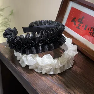 Detailed close-up shot of black and white ruffled rhinestone headbands with shiny fabric.
