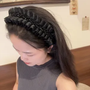 Detail view of the black ruffled beaded headband worn, showing top-crown volume and texture.