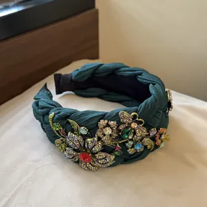 Primo piano dettagliato del cerchietto intrecciato verde scuro con fiori di strass brillanti.