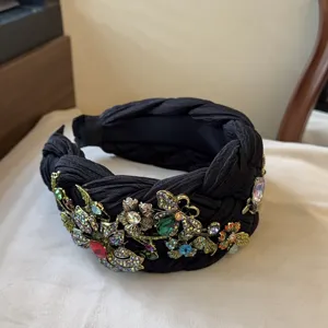 Primo piano del cerchietto intrecciato nero con fiori metallici barocchi e strass colorati.