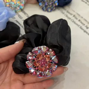 Vue détaillée de l'élastique à cheveux en satin noir avec une fleur de strass multicolore.
