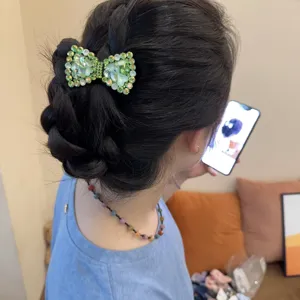 Detail van groene strass strik haarspeld met fonkelende kristallen op elegant gevlochten haar.