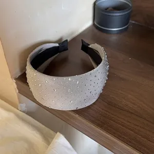 Gedetailleerde opname van een brede zilveren strass haarband, sprankelende kristallen op stof.