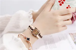 Detail view of a square quartz women watch in coffee gold with steel strap and clover bracelet.