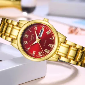 Gros plan d'une montre quartz dorée pour femme avec cadran rouge, chiffres romains et date.