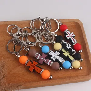 Porte-clés croix en silicone perlé avec design de balles, mousqueton en métal.