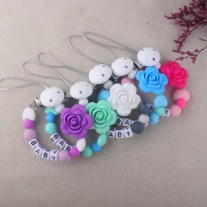 Vista detallada de clips de chupete de silicona coloridos con flores y abalorios de letras.