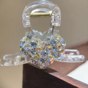 Close-up detail of transparent hair claw clip featuring sparkling heart rhinestones and spring.