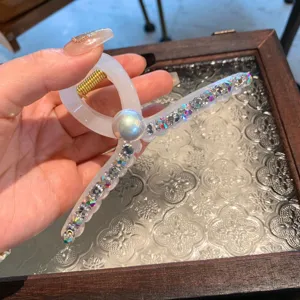 Gros plan d'une grande pince à cheveux en acrylique blanc avec strass colorés et perle.