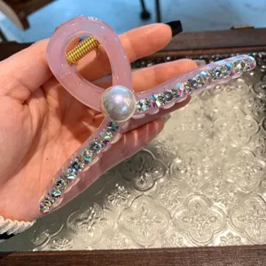 Gros-plan de pince à cheveux en résine rose avec perle et strass scintillants.