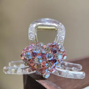 Close-up detail of a clear hair claw clip featuring a sparkly pink rhinestone heart design.