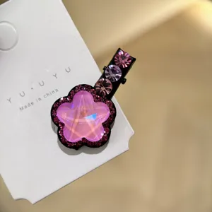 Gros plan d'une pince à cheveux fleur en cristal rose scintillant sur une carte blanche.