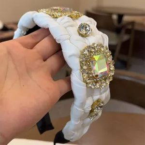 Diadema trenzada blanca con pedrería de brillantes y gran piedra central iridiscente.
